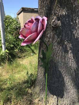 Een kunstwerkje, grote roze roos gemaakt van metaal, op steel